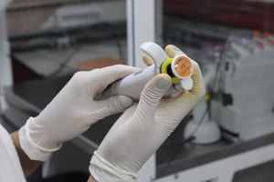 A pair of gloved hands holding a micropipette and twisting it to adjust it.